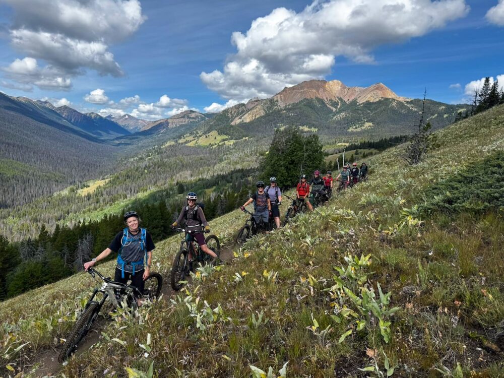group of women on mountain bikes posing on a trail in the alpine meadows with mountains in the background